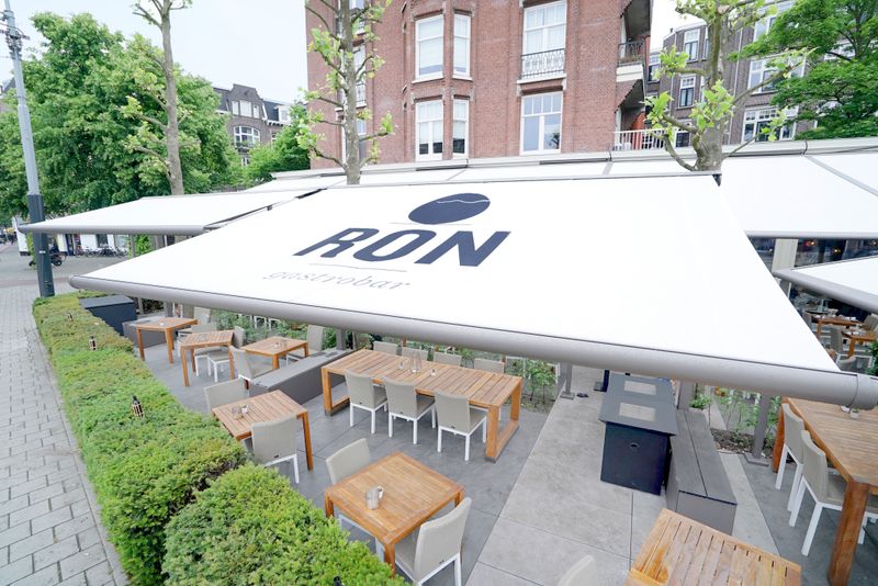 Foto de referencia: toldo cofre markilux 6000 (armazón gris, tejido cofre blanco con impresión del logotipo "Ron gastrobar") - techado de la terraza de un restaurante.